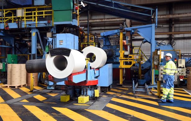 White coils of steel watched by worker wearing high vis, Tata Steel Shotton, North Wales